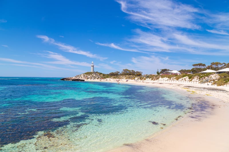Turquoise waters of Pinky's Beach on Rottnest island with beachfront glamping and lighthouse on the headland
