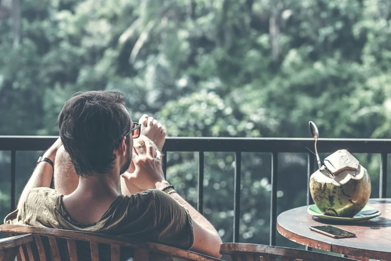 Dude downshifting, one of the blue zones secrets chilling on a balcony with a coconut looking over tropical jungle