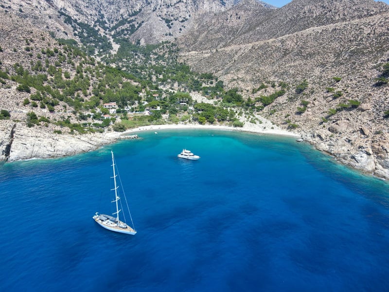 A few yachts anchored in pristine bay of a tiny village in blue zone Ikaria, Greece