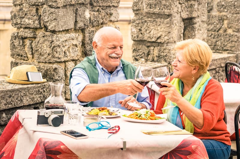 Elderly couple eating Mediterranean food and drinking red wine in alfresco dining