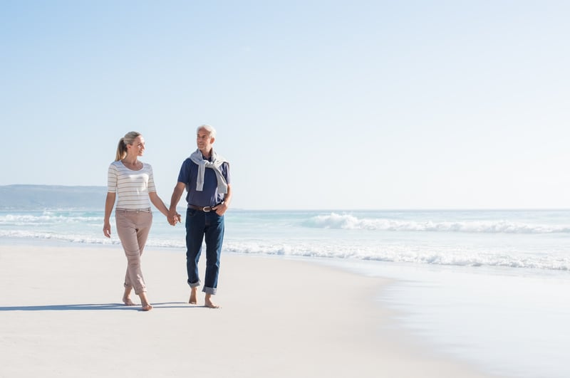 A healthy looking older couple walking along the beach achieving longevity