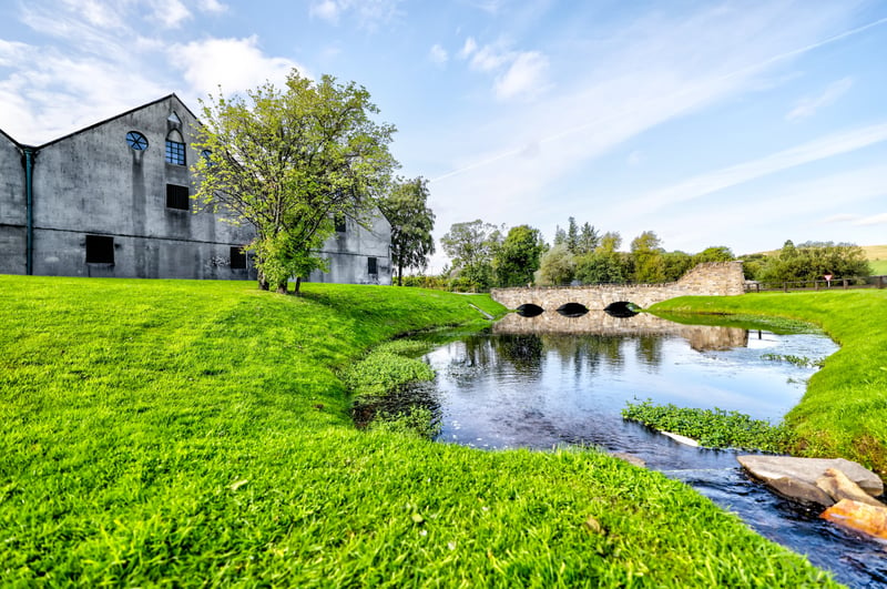 The exterior of Glenlivet Distillery with a lovely creek and stone bridge and green grass in Ballindalloch, Scotland