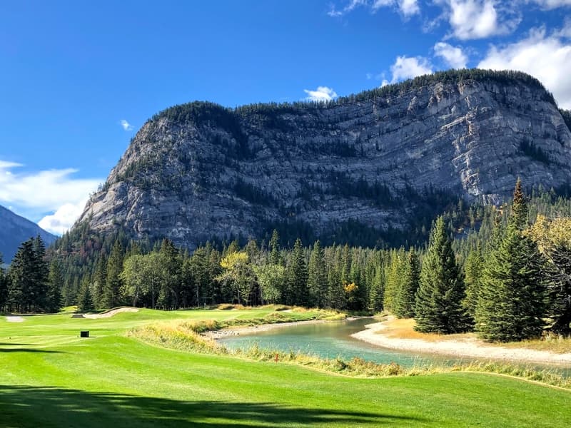 A beautiful view of a par 3 golf hole on a course with mountains in the background