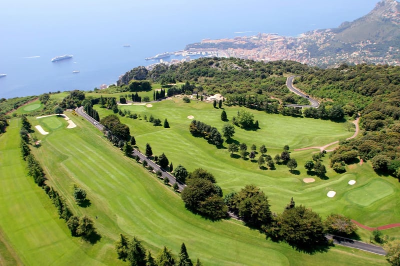 Aerial shot of Monte Carlo Golf Club atop the mountain with the city and Mediterranean below