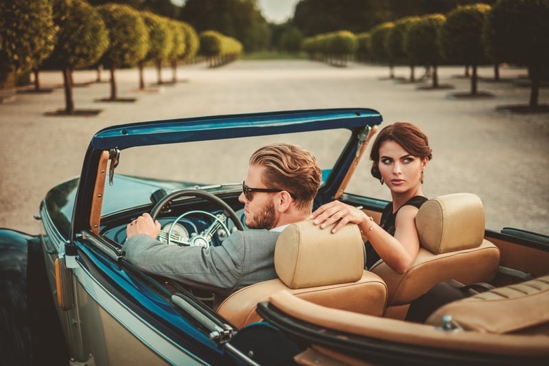 Wealthy couple in classic convertible, a luxury travel experience affluent travelers can book now