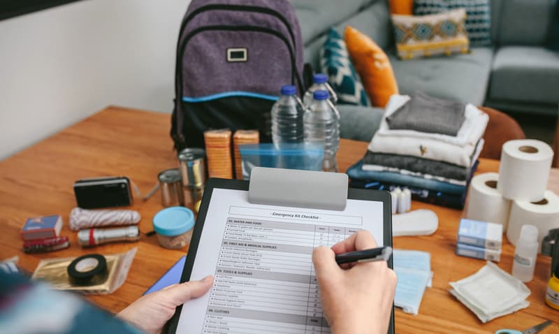 Unrecognizable woman doing checklist of emergency backpack for multi-day trek in the living room