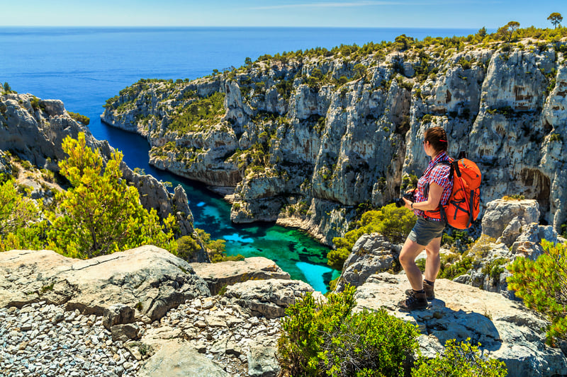 Young hiker woman with backpack and photo camera on the high cliffs,Calanques D En Vau bay,Calanques National Park near Cassis fishing village,Provence,South France,Europe