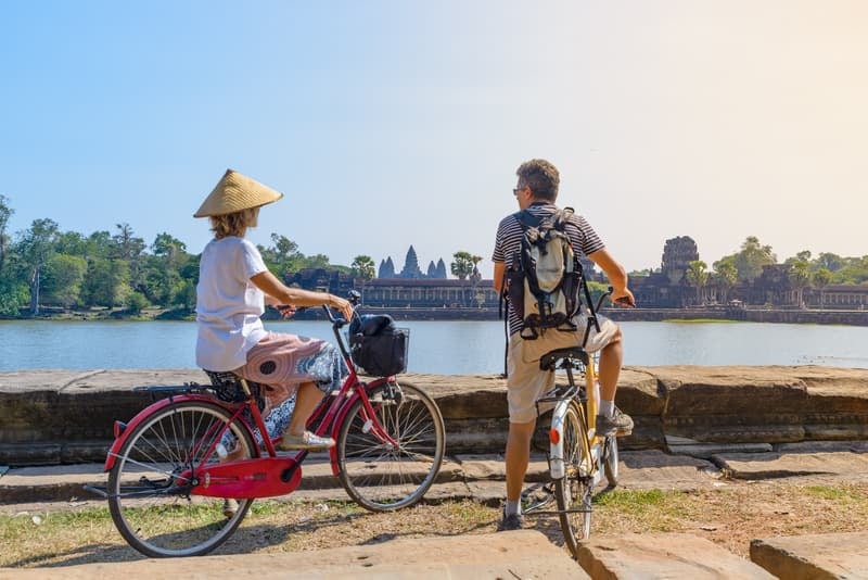 Retired couple on Bicycles looking while traveling and looking across a lake to Angkor Wat, Cambodia