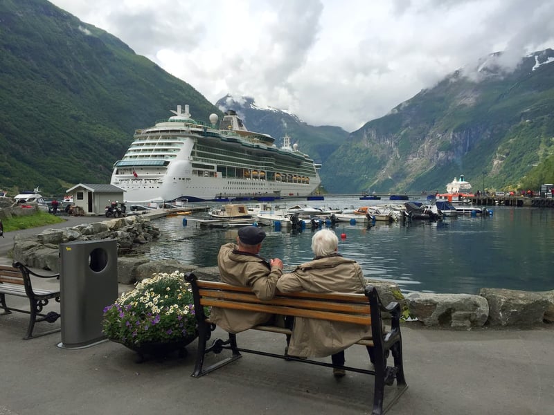 Two elderly men sitting on park bench looking at ship wondering if they can retire on cruise ships