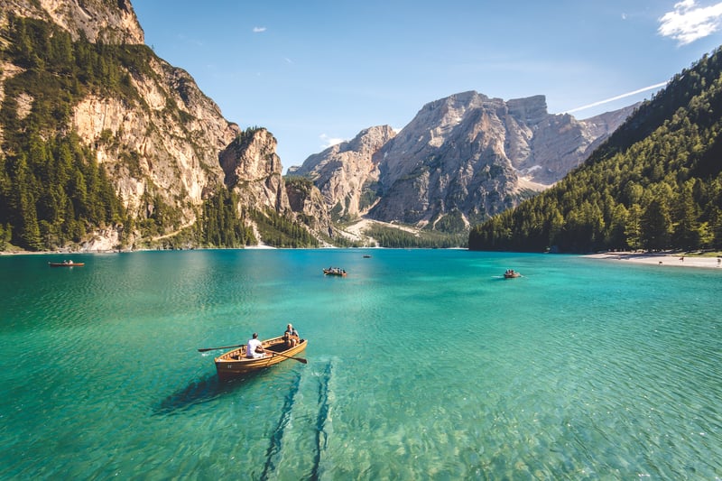 Slow traveling tourists in a row boat in a aqua-marine gorgeous lake with a landscape or nature, mountain and forest in Italy