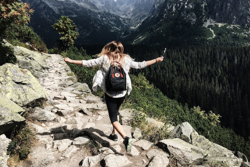 Solo female traveler hiking a trail throwing her arms up in freedom