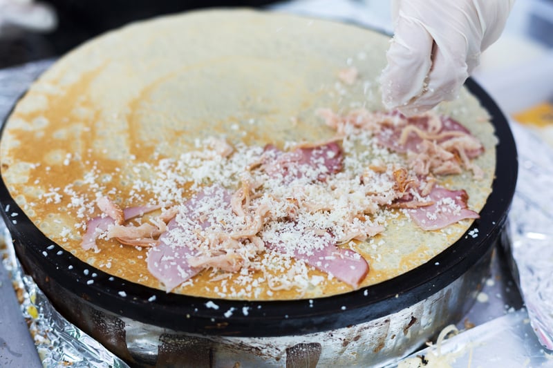 Making ham and cheese crepe at pan. Salty crepe or pancake with fillings made by street vendor`s hands at outdoors creperie. French cuisine, cooking for street food vendor