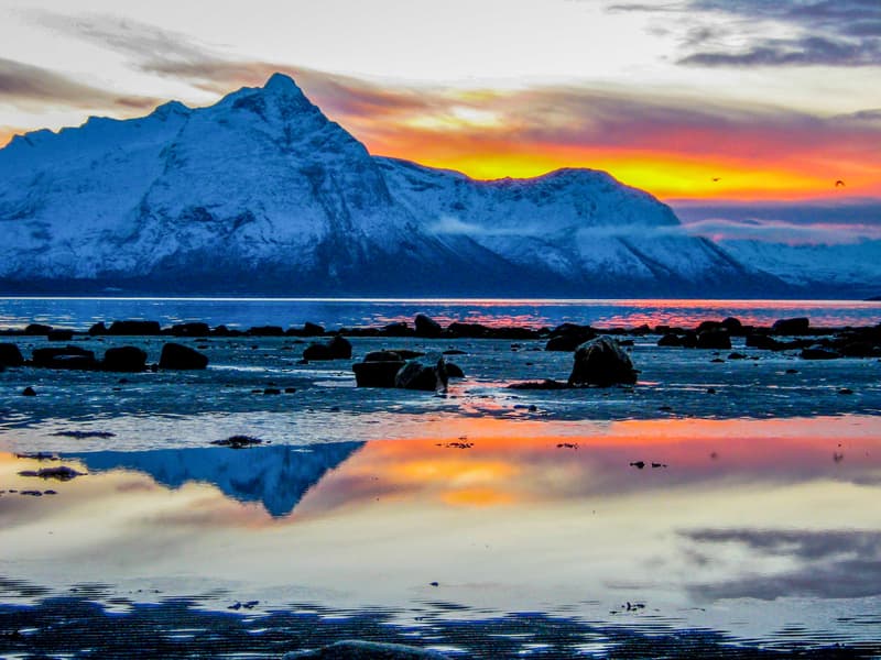 Beautiful sunset over snowcapped mountains reflected off the sea in the Arctic Circle near Scandinavia