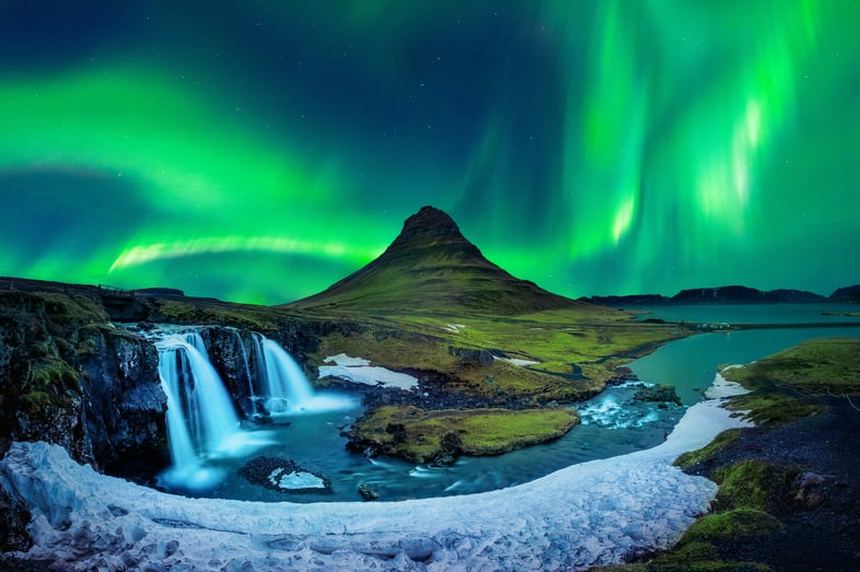 Northern lights over waterfall seen while traveling Scandinavia