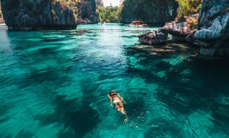 Young woman snorkeling in aquamarine lagoon surrounded by limestone cliffs in El Nido, Palawan, the Philippines