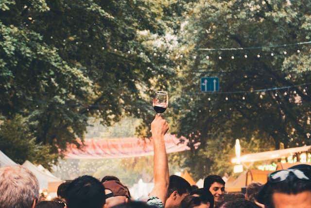 Glass of red wine held up in celebration at a crowded wine festival.