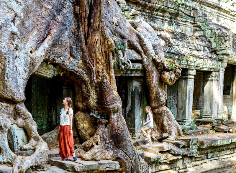 Mother and daughter Worldschooling ancient temples with large tree roots growing over doorways in Angkor Wat, Cambodia