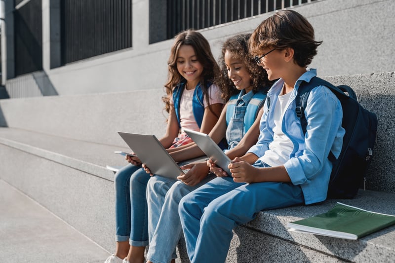 Three kids sitting together on excursion and learning from tablets