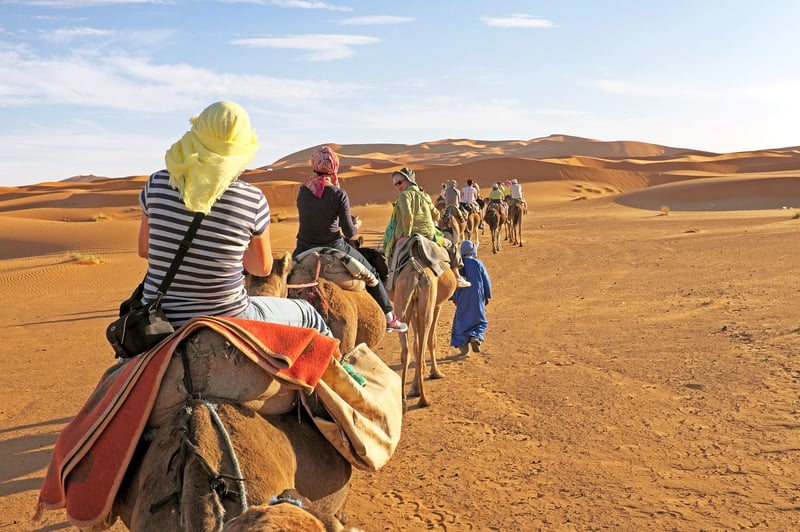 A group of luxury travelers dressed in traditional middle-eastern attire on a cultural camel ride tour on the Sahara desert