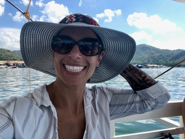Woman living on a boat traveling the world wearing sunglasses and a hat, smiling in the Philippines