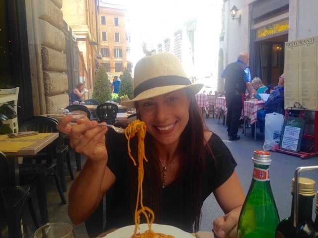 Woman wearing a hat and eating pasta at a street cafe in Rome