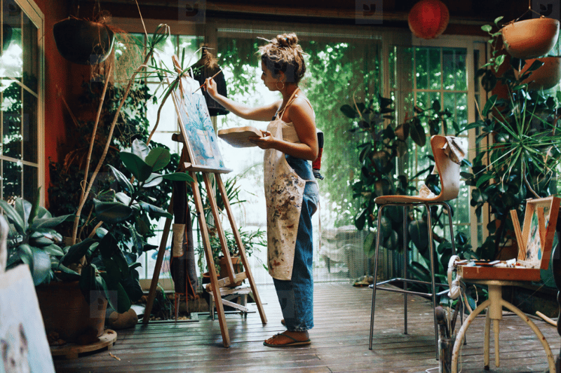 Young woman painting in plant-filled room.