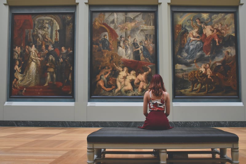 Woman sitting in a museum viewing timeless classic oil paintings.